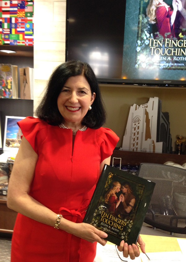 A woman in a red dress smiles while holding a book titled "Ten Fingers Touching" with a romantic cover. A monitor displays the same book cover.